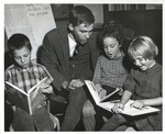 Teacher looking at textbooks with three children by Indiana State University, University Archives